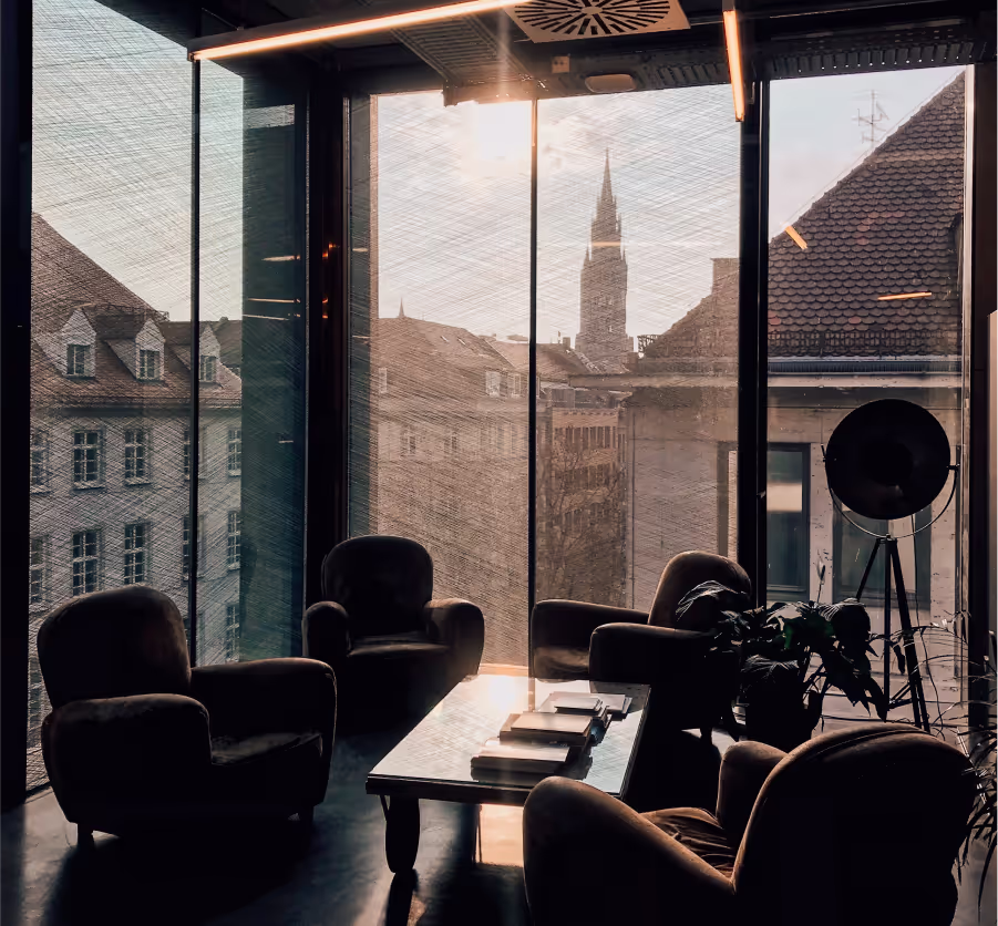 Cozy seating area with armchairs and a coffee table, overlooking a cityscape through large windows at sunset.