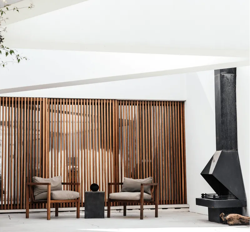 Minimalist outdoor seating area with wooden chairs, a small table, and a modern fireplace.