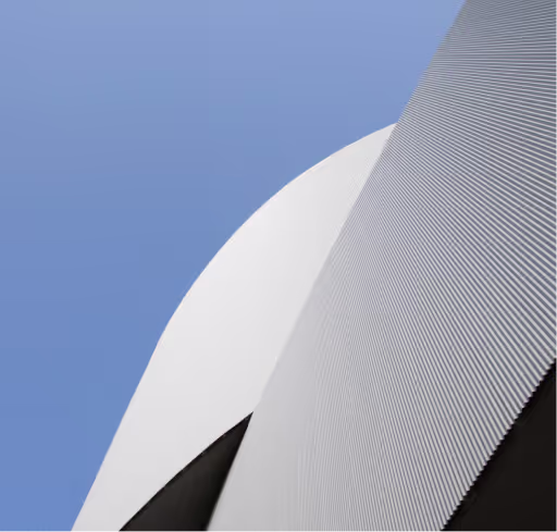 Abstract close-up of a modern building with curved white and textured gray surfaces against a blue sky