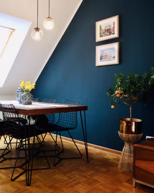 Stylish dining area with a wooden table, wire chairs, pendant lights, and a deep blue accent wall.