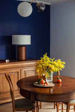 Classic dining setup with a wooden table, yellow flowers in a vase, and a navy blue accent wall.
